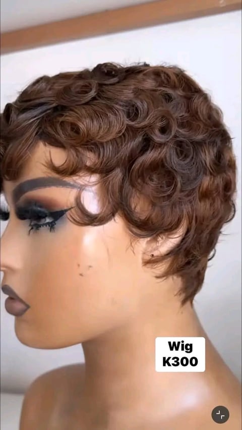 Mannequin head wearing K300 short curly brown wig with side-swept styling and dark makeup, shown in profile view