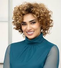 Portrait of a smiling woman with curly blonde hair wearing a teal turtleneck